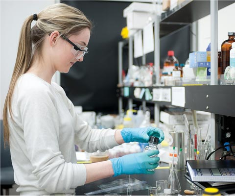 A Young female working in a lab with eye protector glasses and gloves 