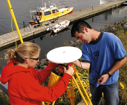 Female and male researchers installing a dish instrument near the river in Fredericton, NB.