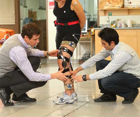Two male researchers adjusting wires on the leg of a female runner.