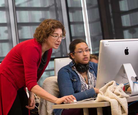 Une professeure enseigne à une étudiante devant un ordinateur Mac.