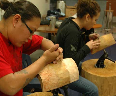 Two Indigenous female artists carving wood sculptures.
