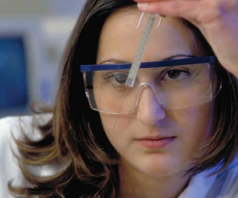 Jeune chercheuse portant des lunettes protection regarde une aiguille.