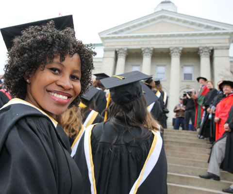 Étudiante noire souriante habillée en toge faisant la queue lors de la cérémonie de la remise des diplômes.