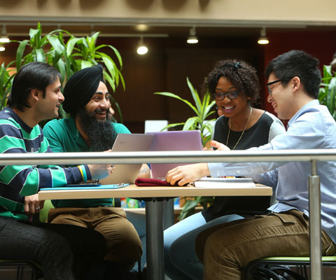 Students from different ethnic backgrounds study together at a cafeteria table.