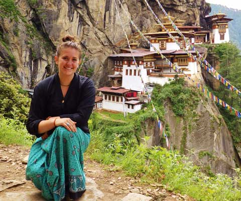 Smiling female student in front of hillside village in Bhutan.