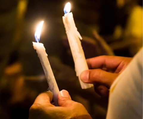 Two lit candles are being held at a vigil at nighttime.