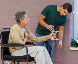Male student testing a hand strength instrument with an elderly man in a wheelchair.