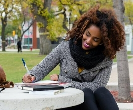 Sur un campus universitaire, une jeune femme étudie à une table extérieure.
