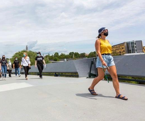 A group of university students wearing masks and face coverings walk across a bridge on the Trent University campus.