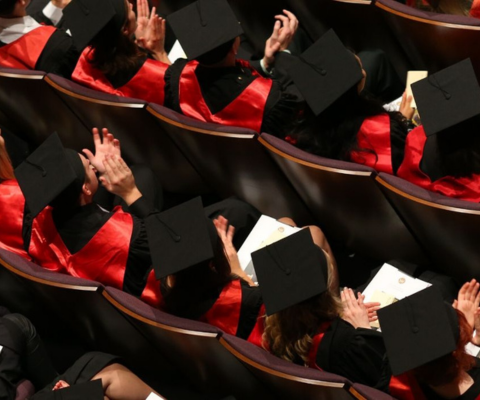 Students sitting in an auditorium, clapping during a convocation ceremony.