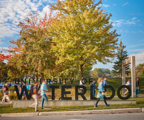 University of Waterloo campus sign with students walking by.
