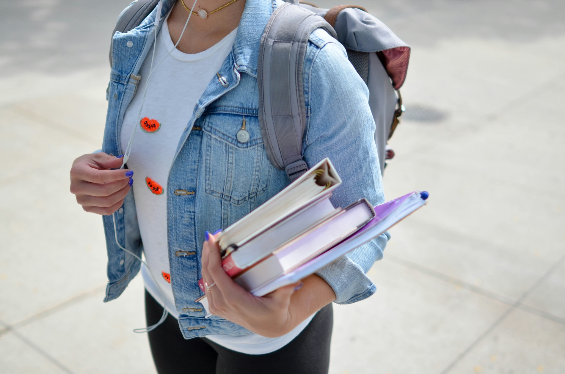 Close up of student holding books wearing a backpack with headphones in