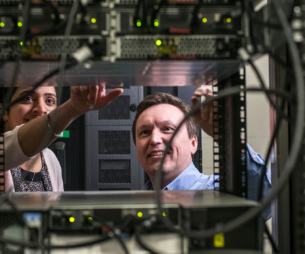 Two people working on a server with wires and electronics