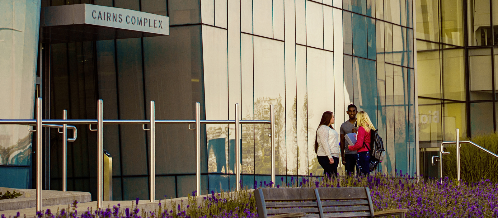 Three student standing outside a research complex building on a university campus.