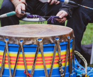 Three people around a drum holding drumsticks.