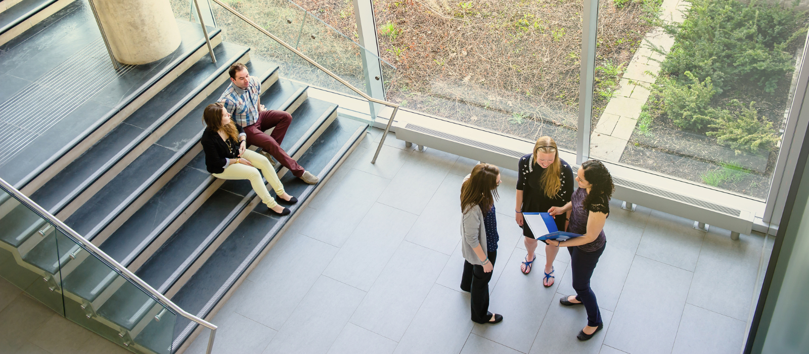 Two students sitting on stairs talking and three students standing and speaking