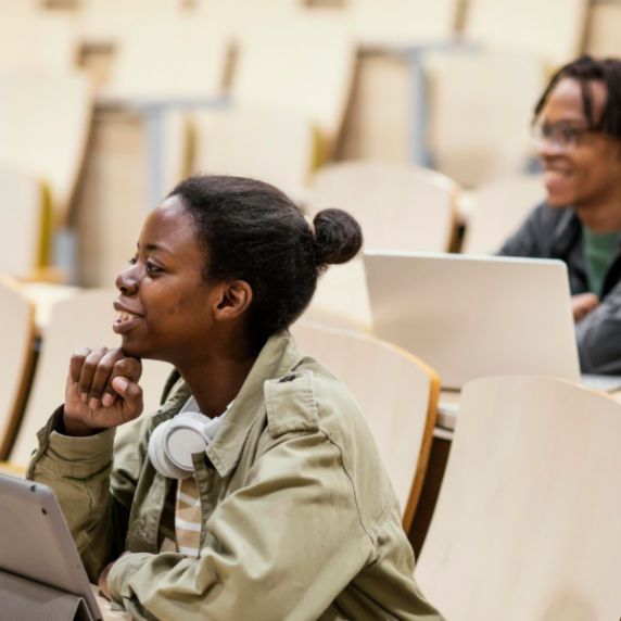 Two students on tablet and laptop in classroom setting