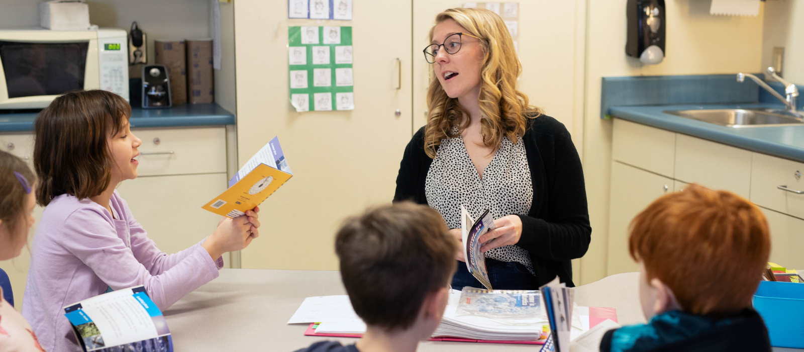 A teacher and children sitting around a table reading books together