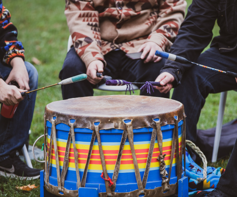 Three people around a drum holding drumsticks / Trois personnes autour d'un tambour tenant des pilons.