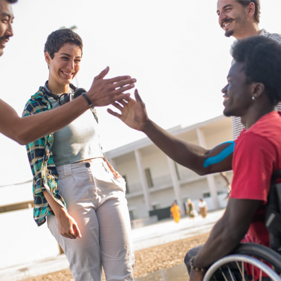 Four young people, one in a wheelchair, smiling and giving high-fives.