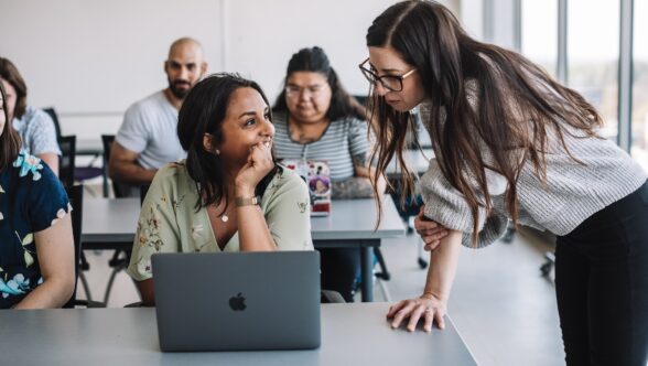 A student showing something on her computer to her professor