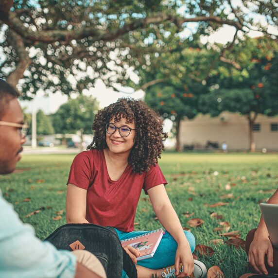 Group of three students outside sitting in a circle studying with a notepad and laptop