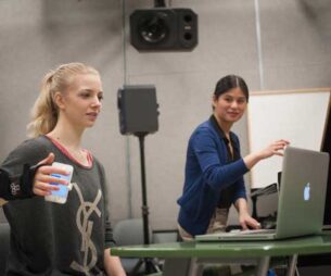 Two student researchers working with a laptop and a cell phone in a lab.