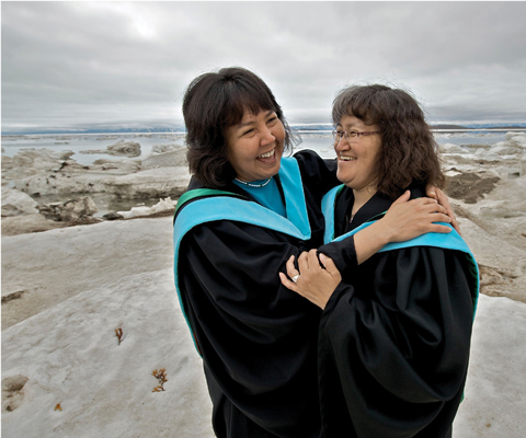 Two people wearing robes standing outside on rocks with lake in background