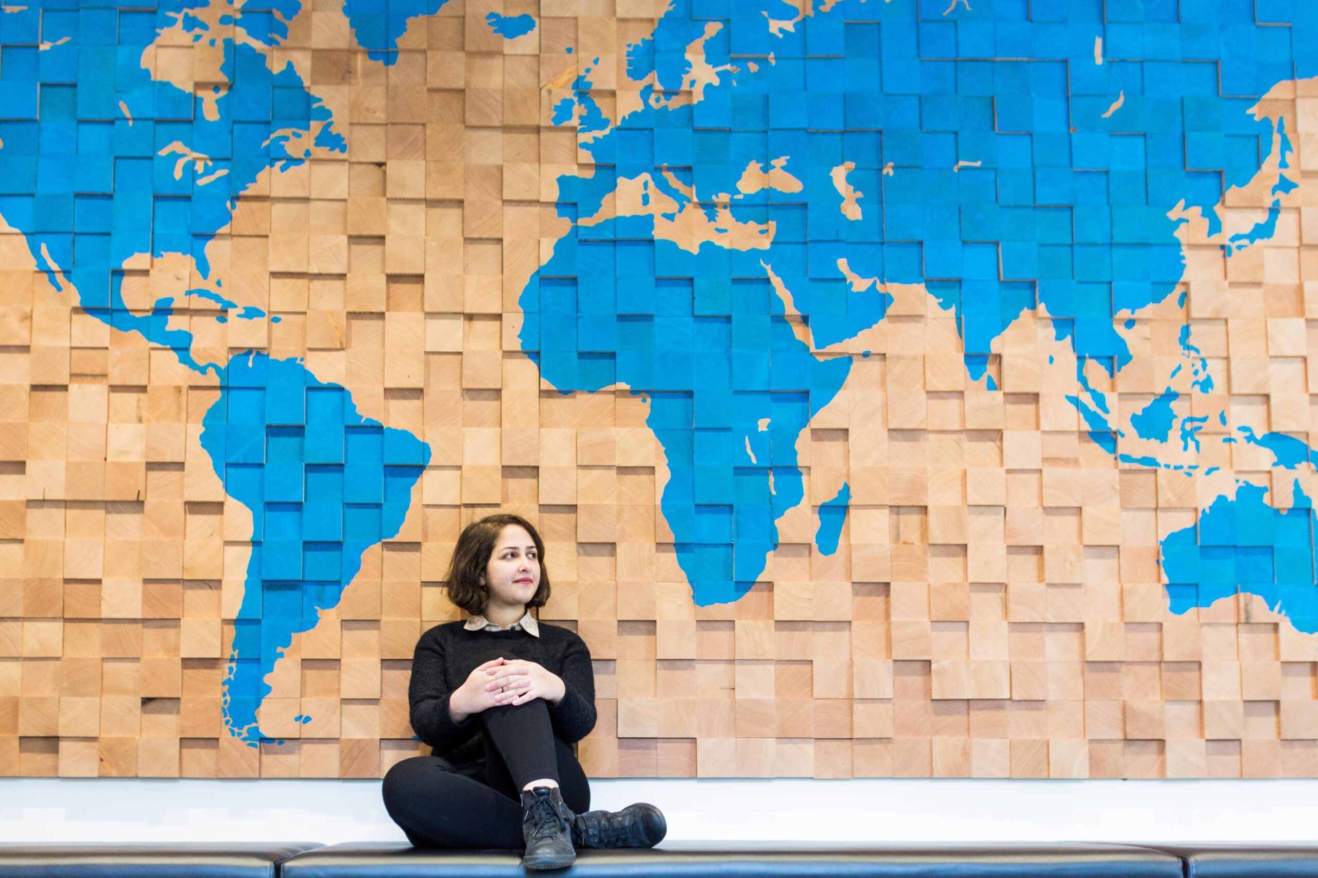 Student sitting by a wall with with a large map on it.