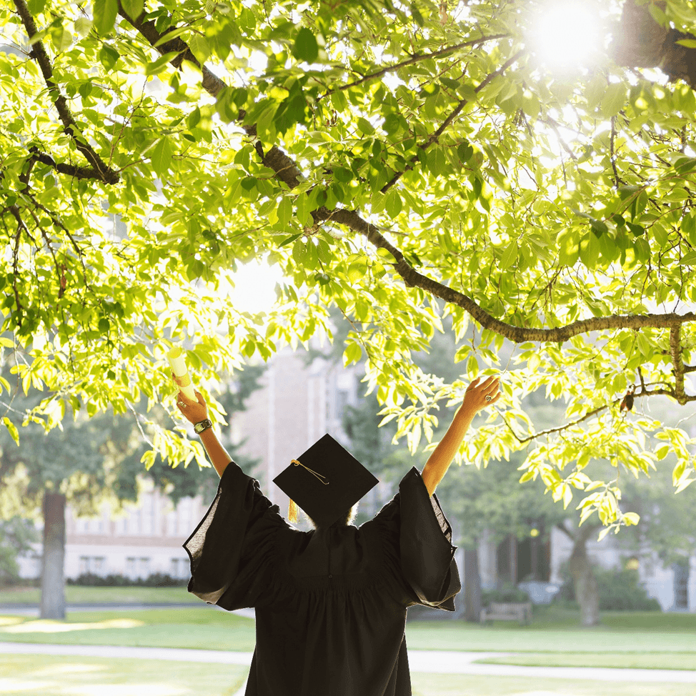 Image d'un étudiant en toge de remise des diplômes levant les mains en signe de joie à l'extérieur.