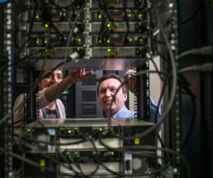 Deux personnes travaillant sur un rack d'équipement dans une salle de serveurs où les câbles sont très nombreux.