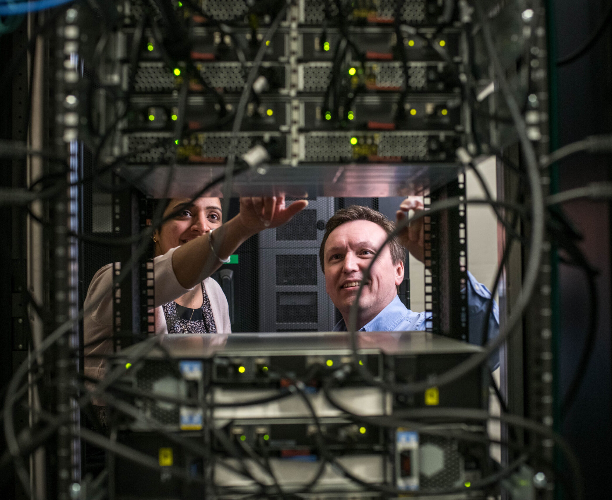 Deux personnes travaillant sur un rack d'équipement dans une salle de serveurs où les câbles sont très nombreux.