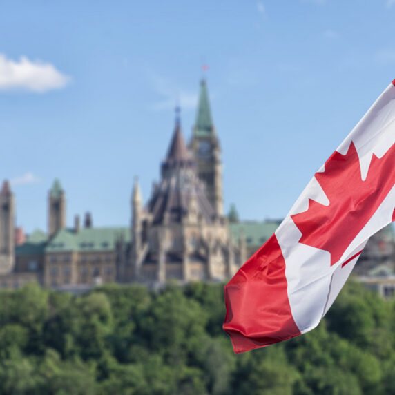 Canadian flag waving with Parliament Buildings hill and Library in the background.