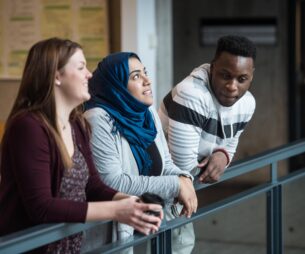 Un groupe de trois étudiants d'horizons différents, penchés sur une balustrade, en train de discuter.