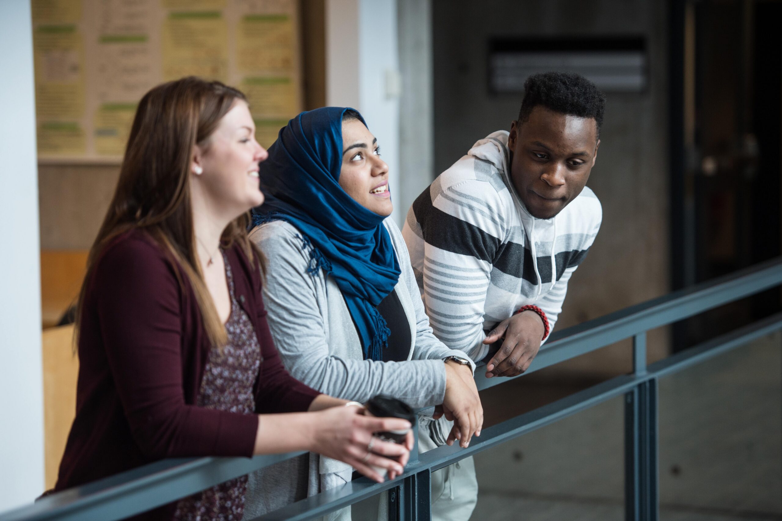 Un groupe de trois étudiants d'horizons différents, penchés sur une balustrade, en train de discuter.